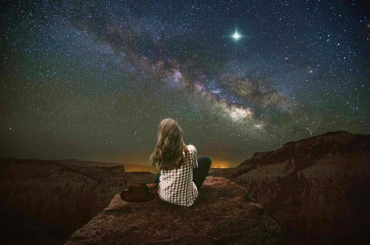 Young woman sitting on rock under stars